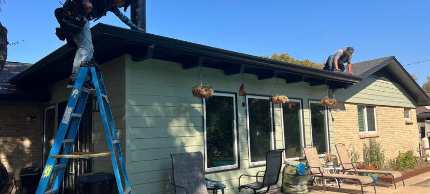 2 men on a roof, one with a ladder cleaning gutters on a house in Austin Texas